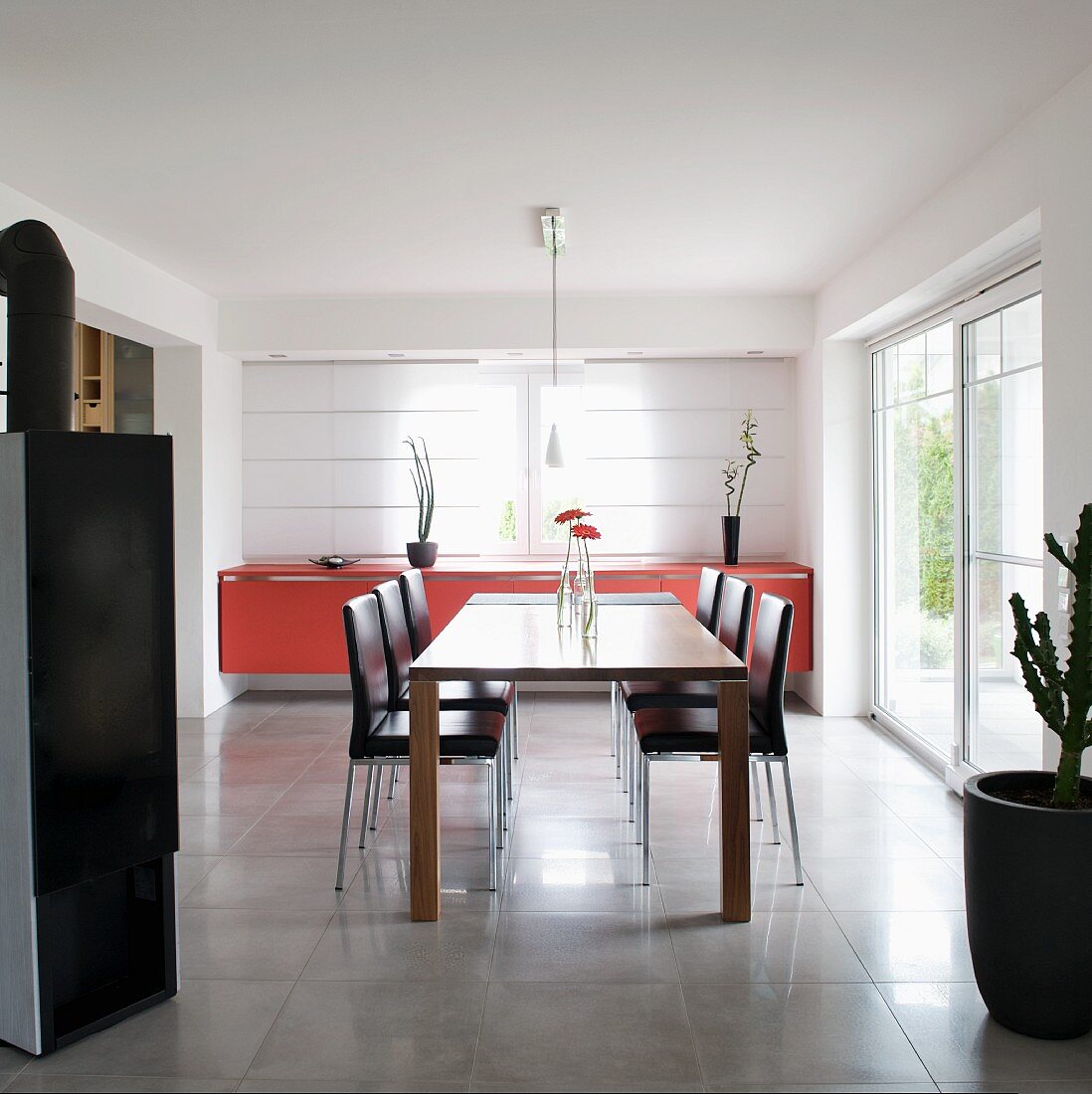 Moderner Esstisch und lederbezogene Stühle vor Sideboard mit roter Front am Fenster mit geschlossenen Flächenvorhängen