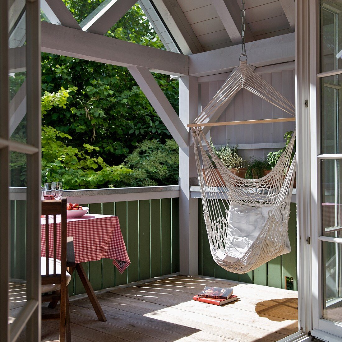 Relaxing in a hammock - view of sunny balcony through open door of wooden house