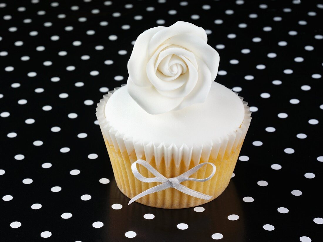 A cupcake decorated with a white rose and a ribbon