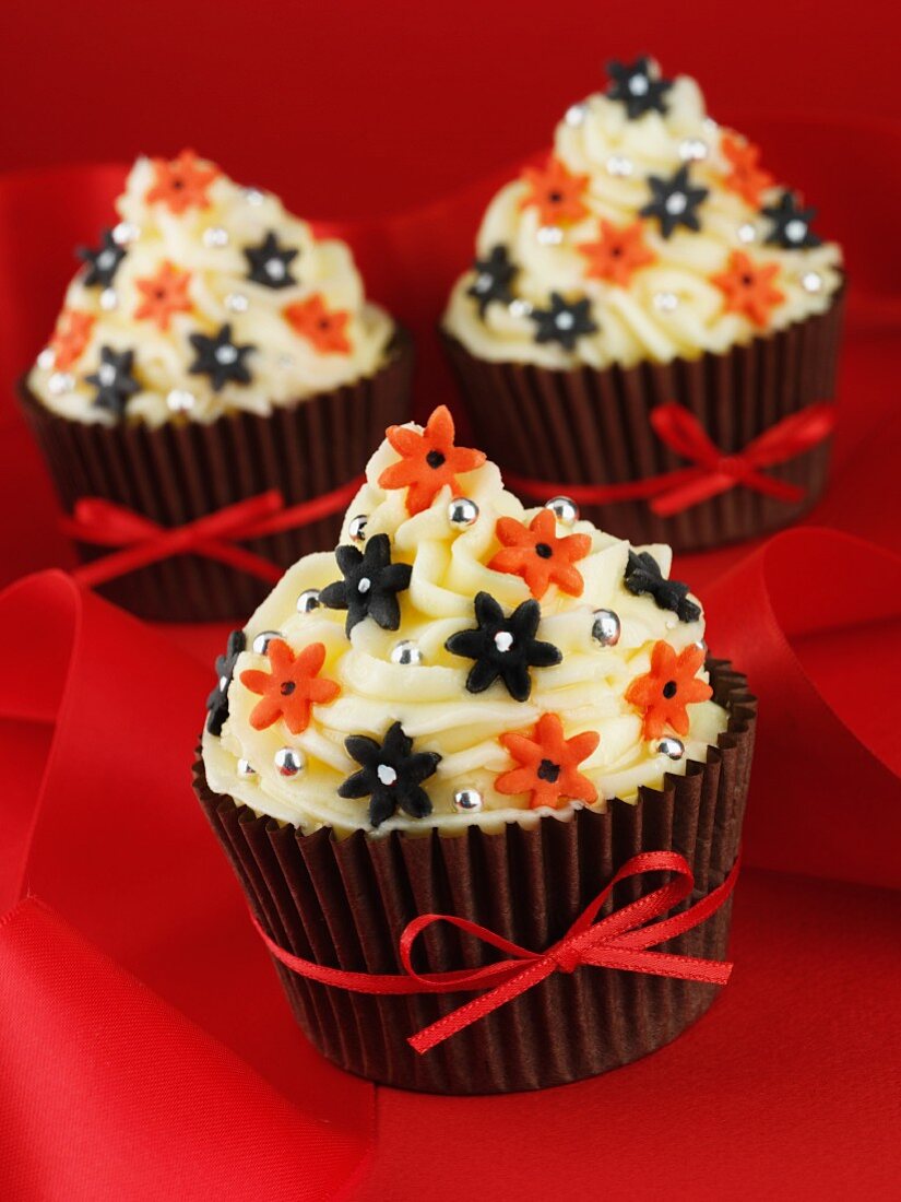 Cupcakes decorated with buttercream, sugar flowers and a red ribbon
