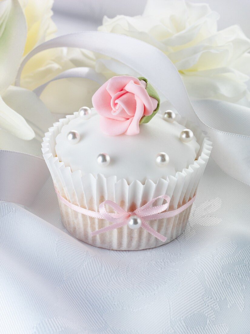 A wedding cupcake with a pink sugar rose and silver balls