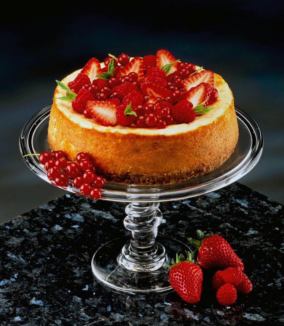 A baked cheesecake with strawberries and redcurrants on a cake stand