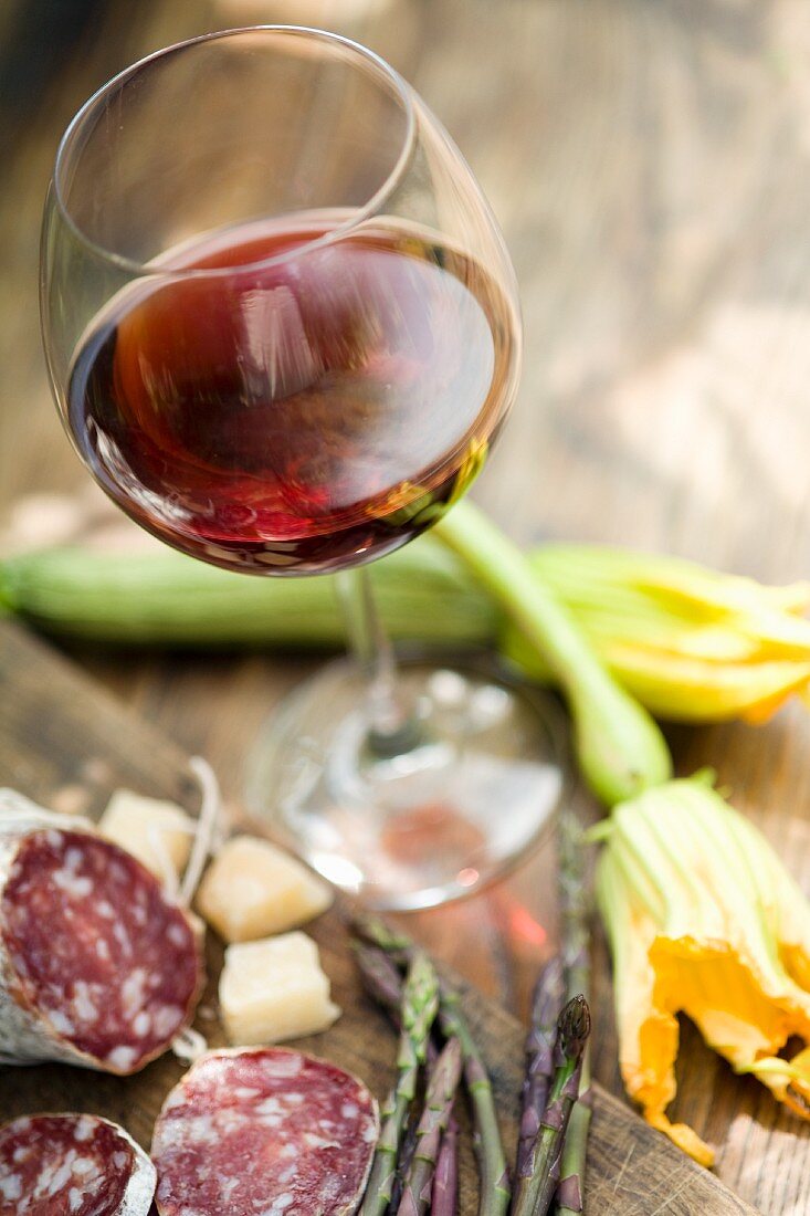 Stillleben mit einem Glas Rotwein, Zucchiniblüten und Salami