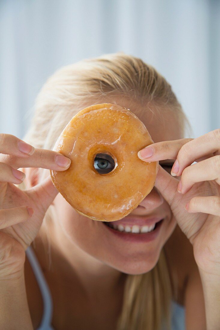 A blonde woman looking through a ring doughnut