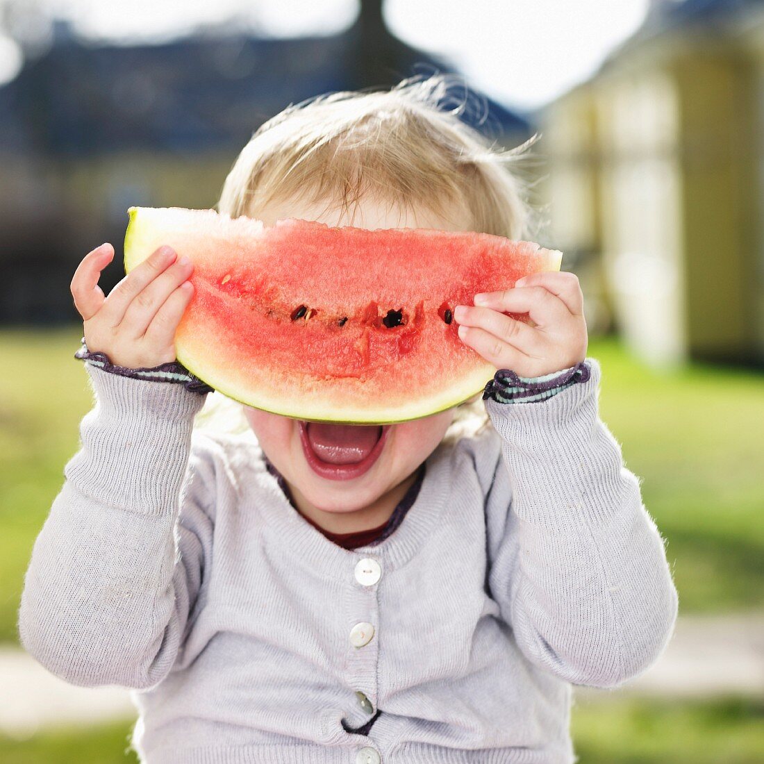 A little girl hiding behind a slice of watermelon