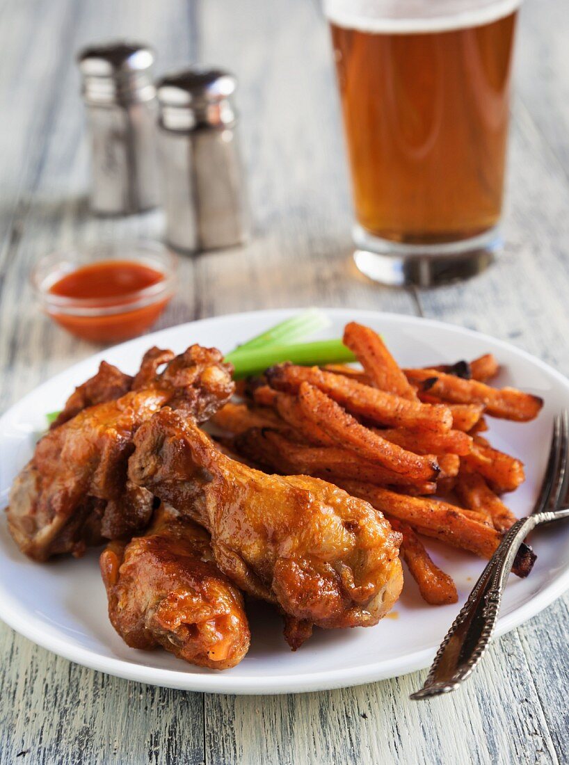 Buffalo Chicken Wings with Sweet Potatoes Fries, Celery Sticks and a Glass of Beer