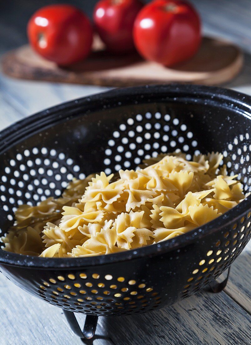 Uncooked Farfalle Pasta in an Old Colander with Tomatoes in the Background