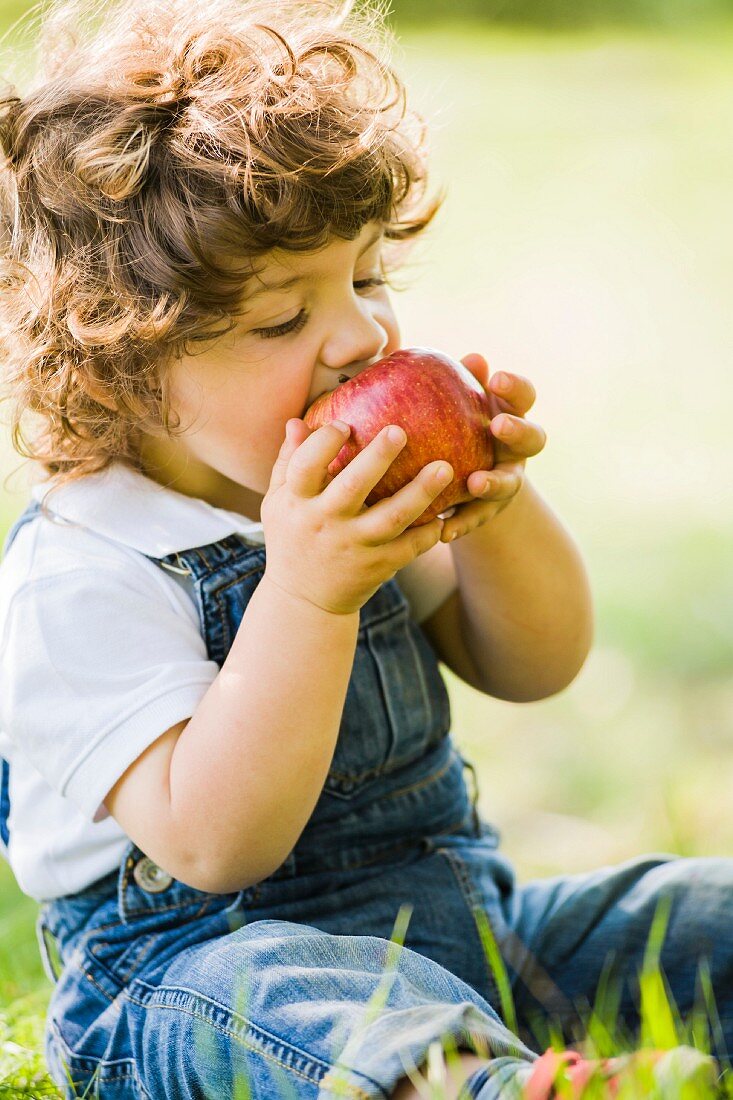Kleiner Junge isst einen großen Apfel
