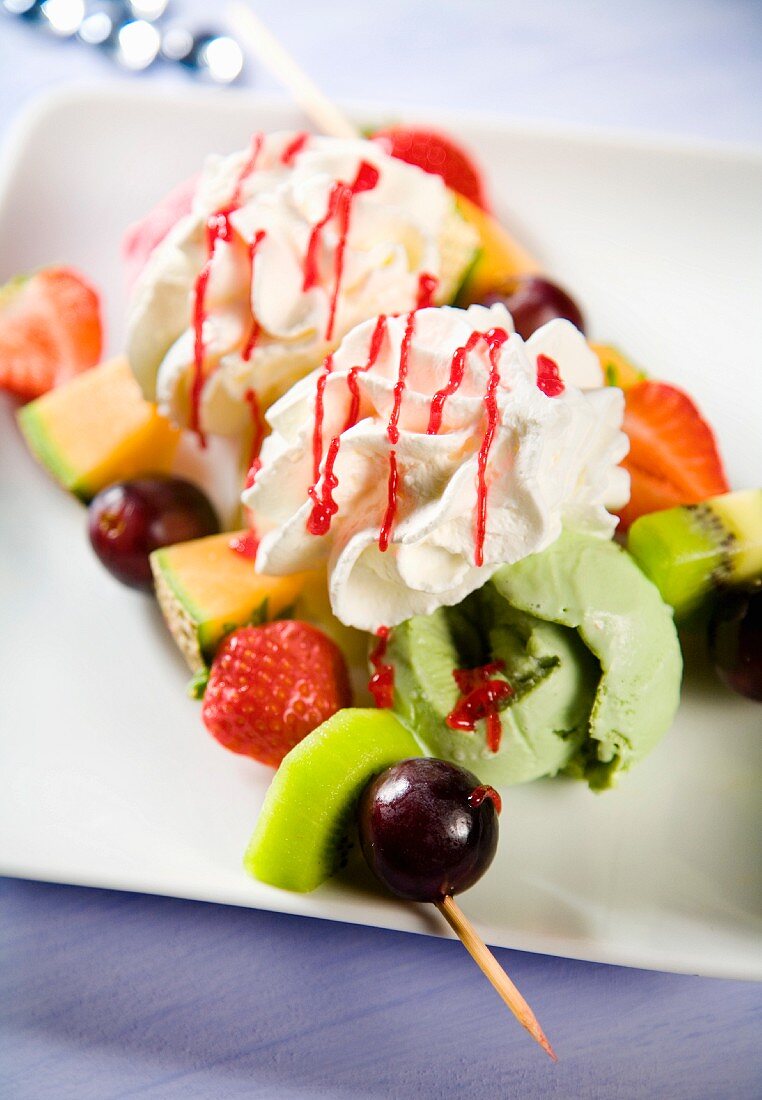 Pistachio ice cream with fruit skewers, whipped cream and strawberry sauce