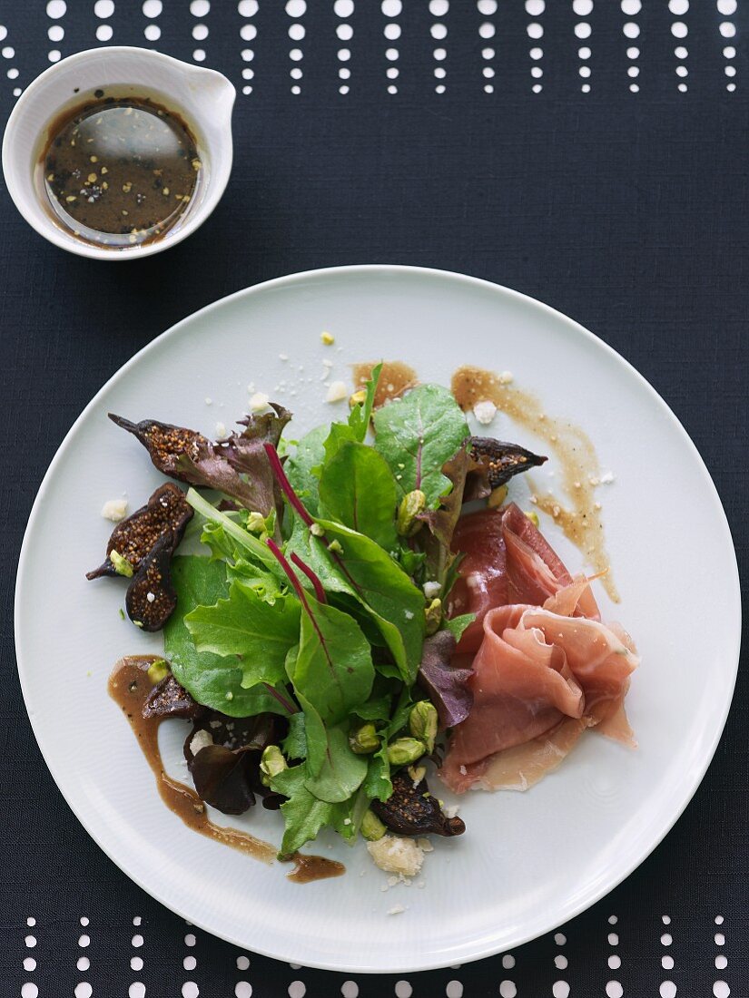 Mixed Green Salad with Prosciutto, Dry Figs, Pistachios and Balsamic Vinaigrette; On a White Plate; From Above