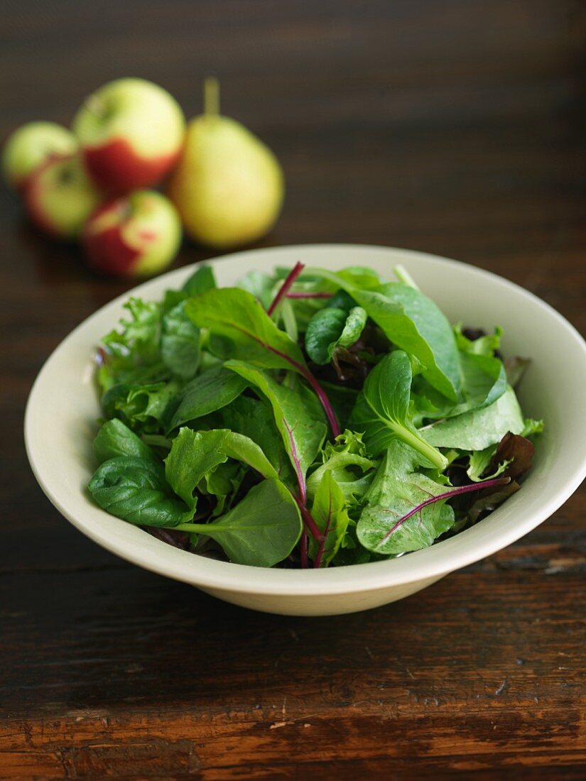 A Bowl of Organic Mixed Green with Apples and Pears in the Background