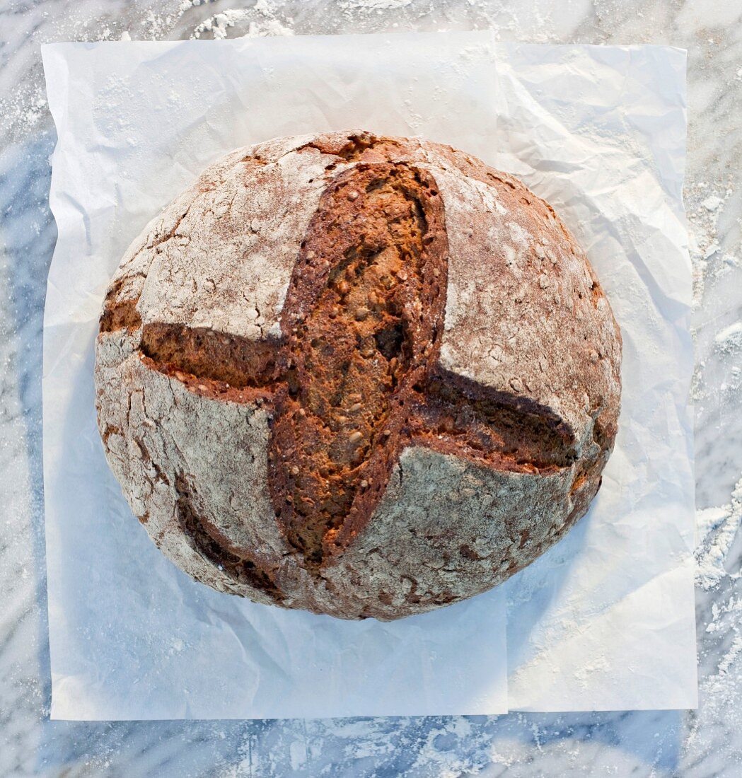 A rustic loaf of bread on paper, on a marble slab, dusted with flour