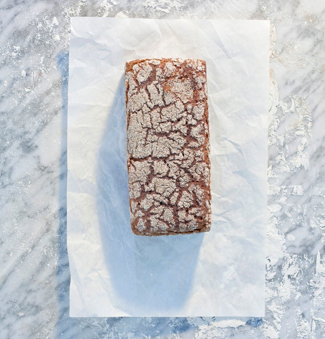 A wholemeal sandwich loaf on paper, on a marble slab, dusted with flour