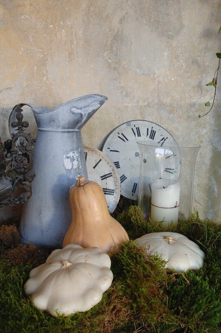 Antique water jug, old clock faces and pumpkins on bed of moss as romantic country house decoration