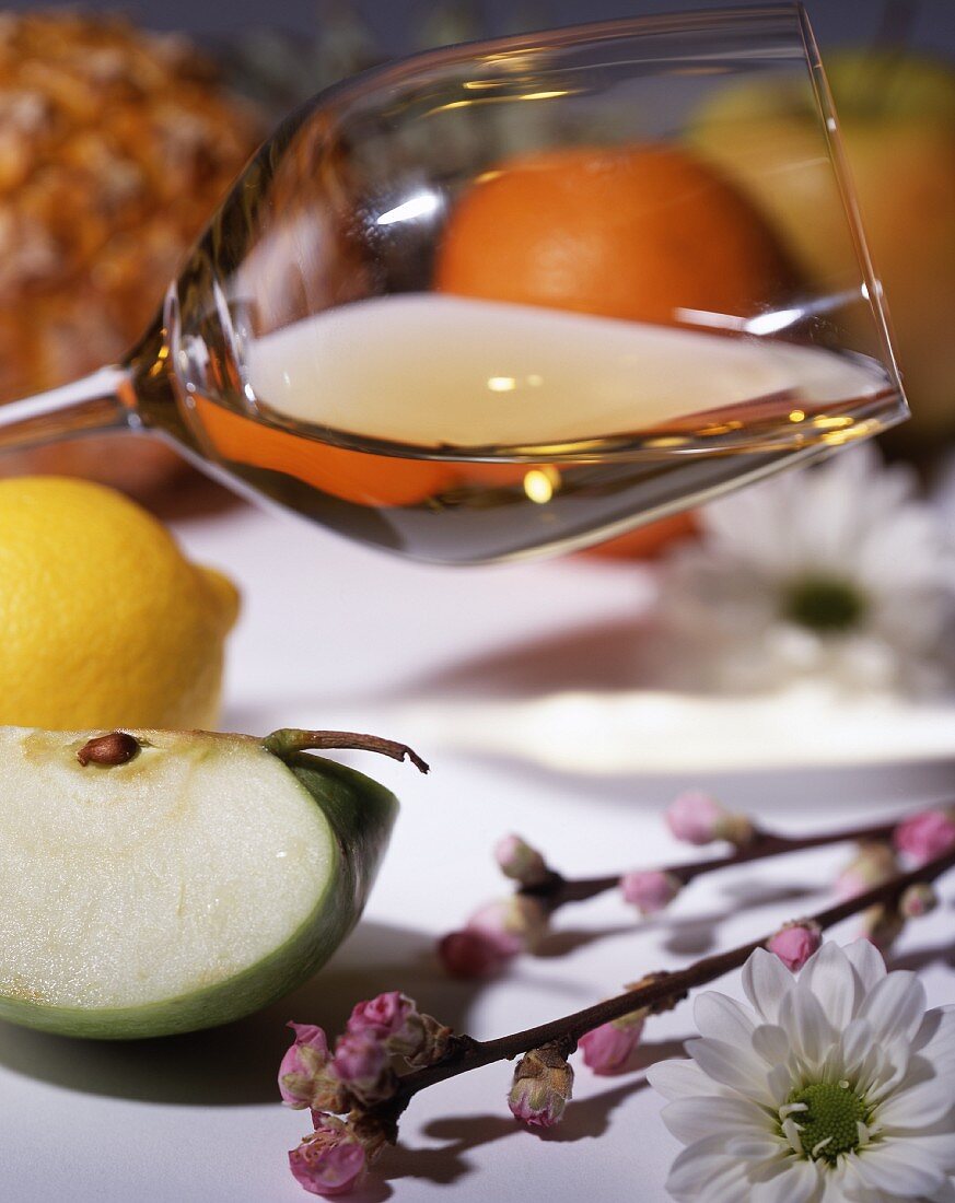 A glass of white wine, with fruits and flowers