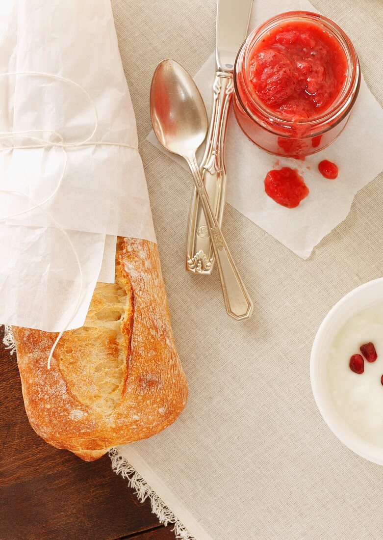 Erdbeermarmelade, Baguette & Joghurt auf Tisch (Aufsicht)