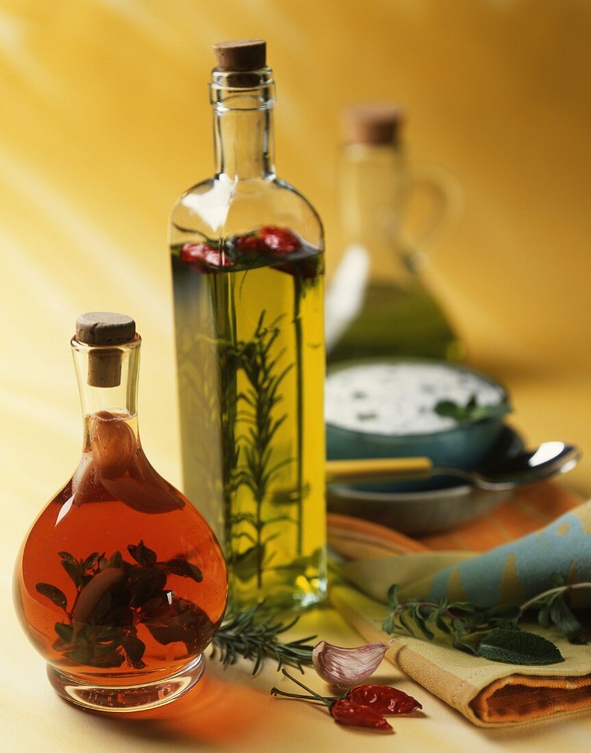 Aromatisiertes Öl und aromatisierter Essig in Flaschen; im Hintergrund eine Kräutersauce