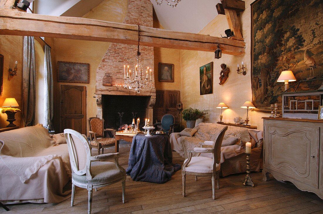 Rococo-style armchair and sofa around table draped with table cloth in rustic living room with exposed wooden beams