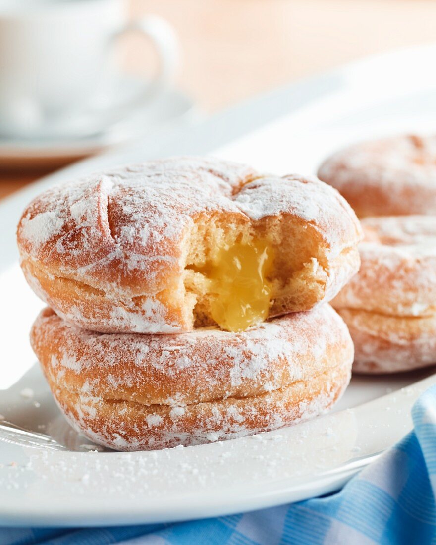 Lemon Jelly Filled Powdered Doughnuts on a White Dish; One Bitten with Jelly Oozing Out