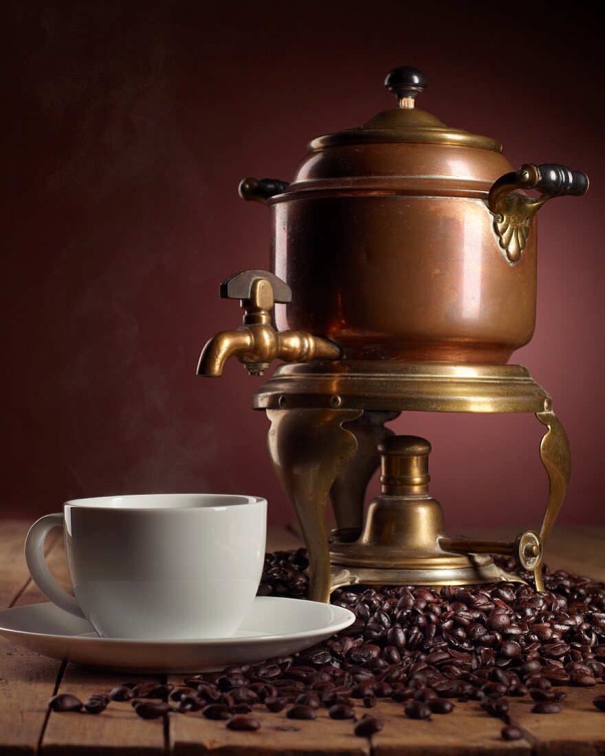 Antike Kaffeemaschine mit dampfender Kaffeetasse und vielen Kaffeebohnen
