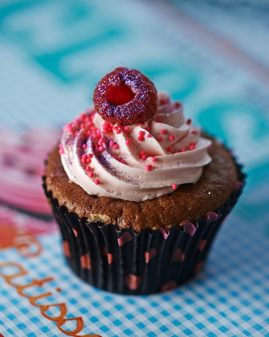 A cupcake topped with icing and a raspberry