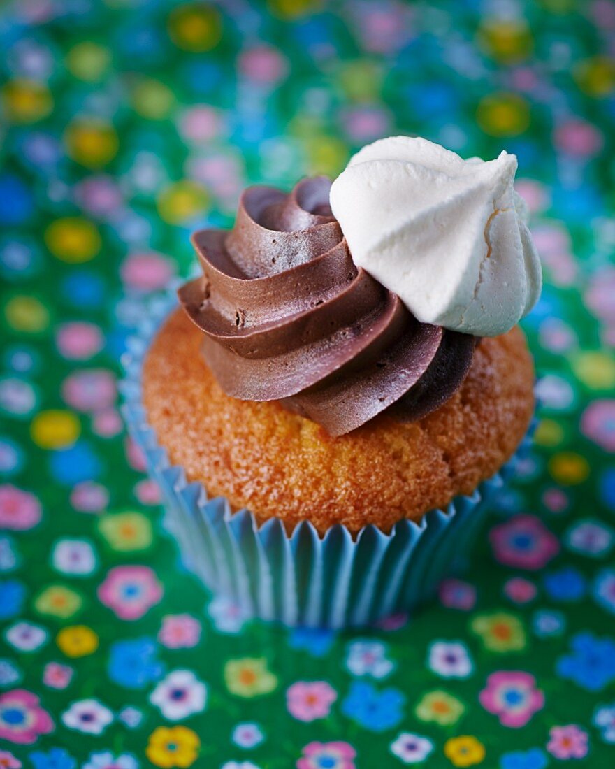 A cupcake topped with chocolate cream and a mini meringue