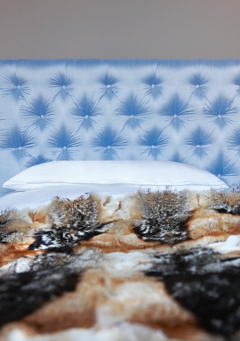 Bett mit Tierfelldecke und einem Kopfteil aus hellblauem Satin mit Polsterknöpfen