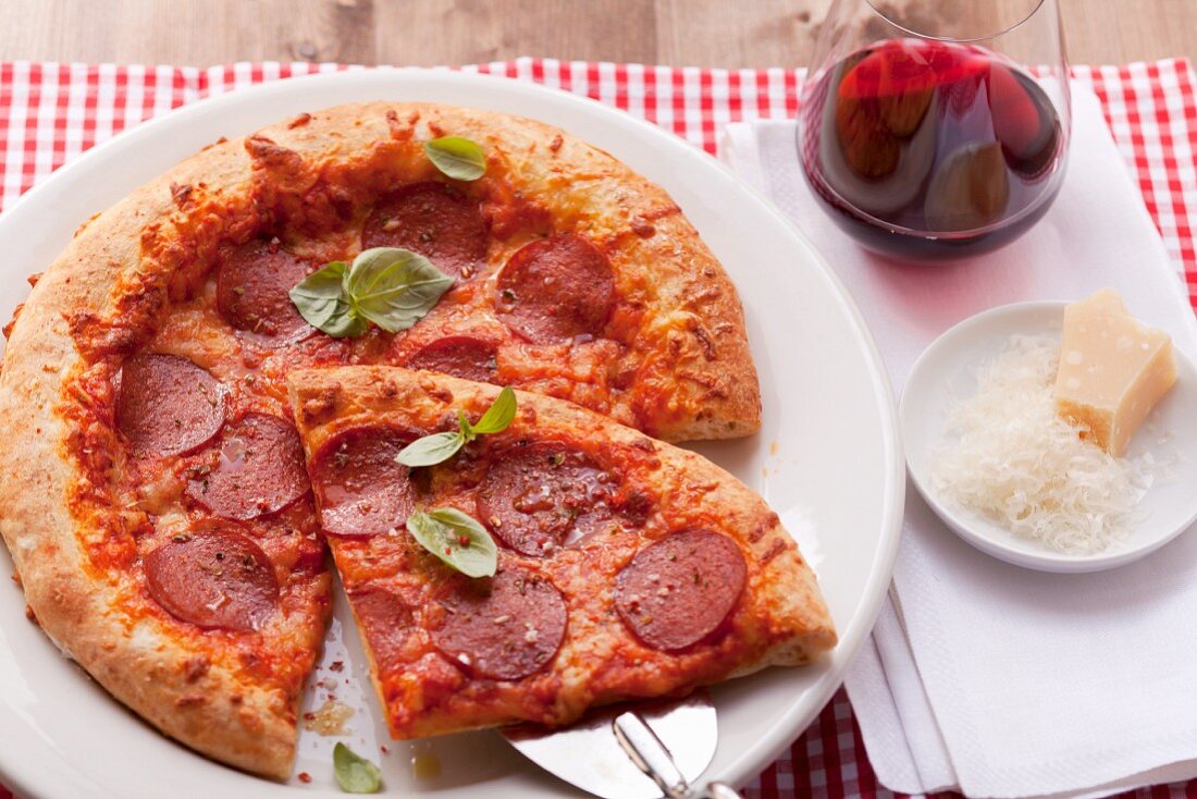 Pizza mit Salami und Basilikum, ein Stück auf Heber