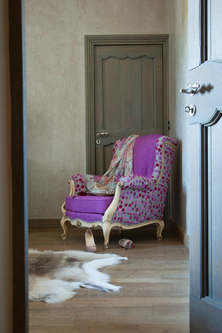 View through open door of Rococo-style reading chair with colourful, spotted designer upholstery in corner of room against door