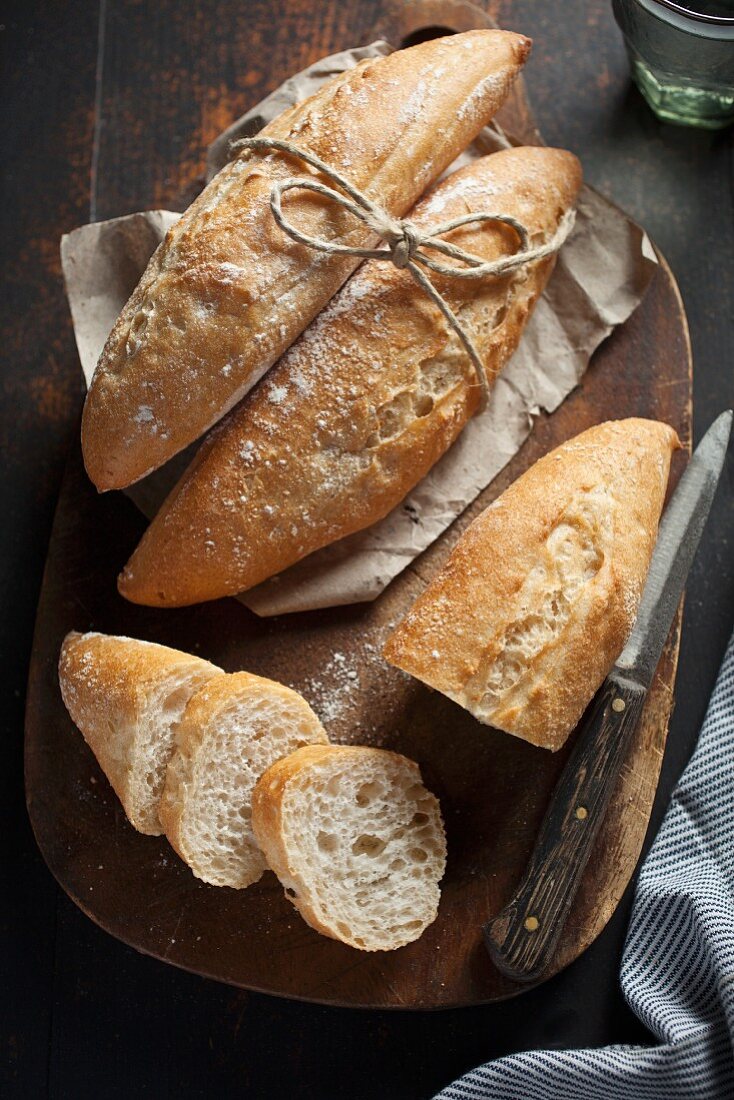 Small baguette rolls, whole and sliced, on a wooden board