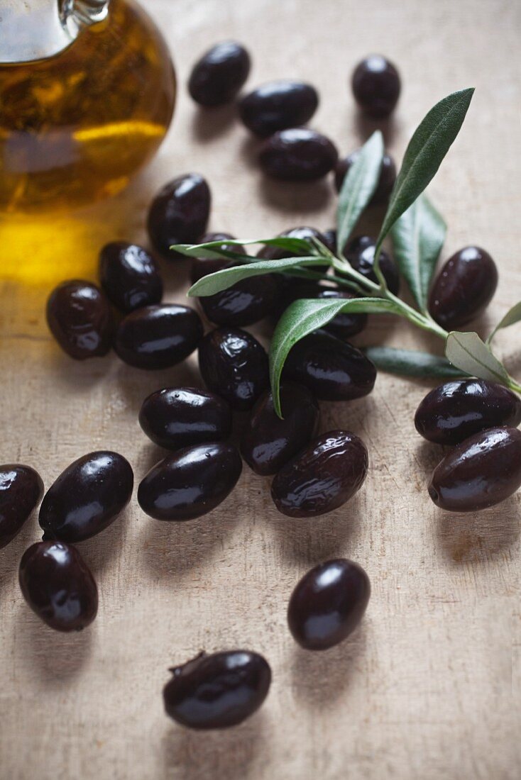 A still life of black olives, a small olive branch and olive oil