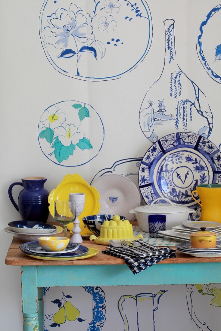 Blue, white and yellow crockery on a table against a wall poster decorated with a crockery motif in the same colours