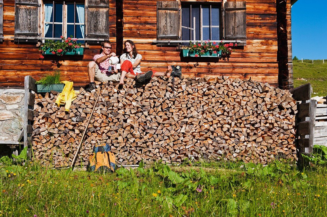 Paar sitzt auf einem Brennholzstapel bei einem Holzhaus