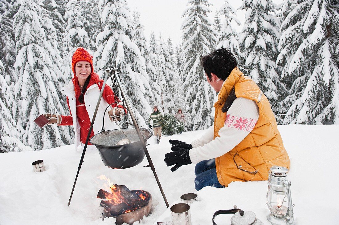 Couple cooking Christmas dinner over campfire in snowy forest