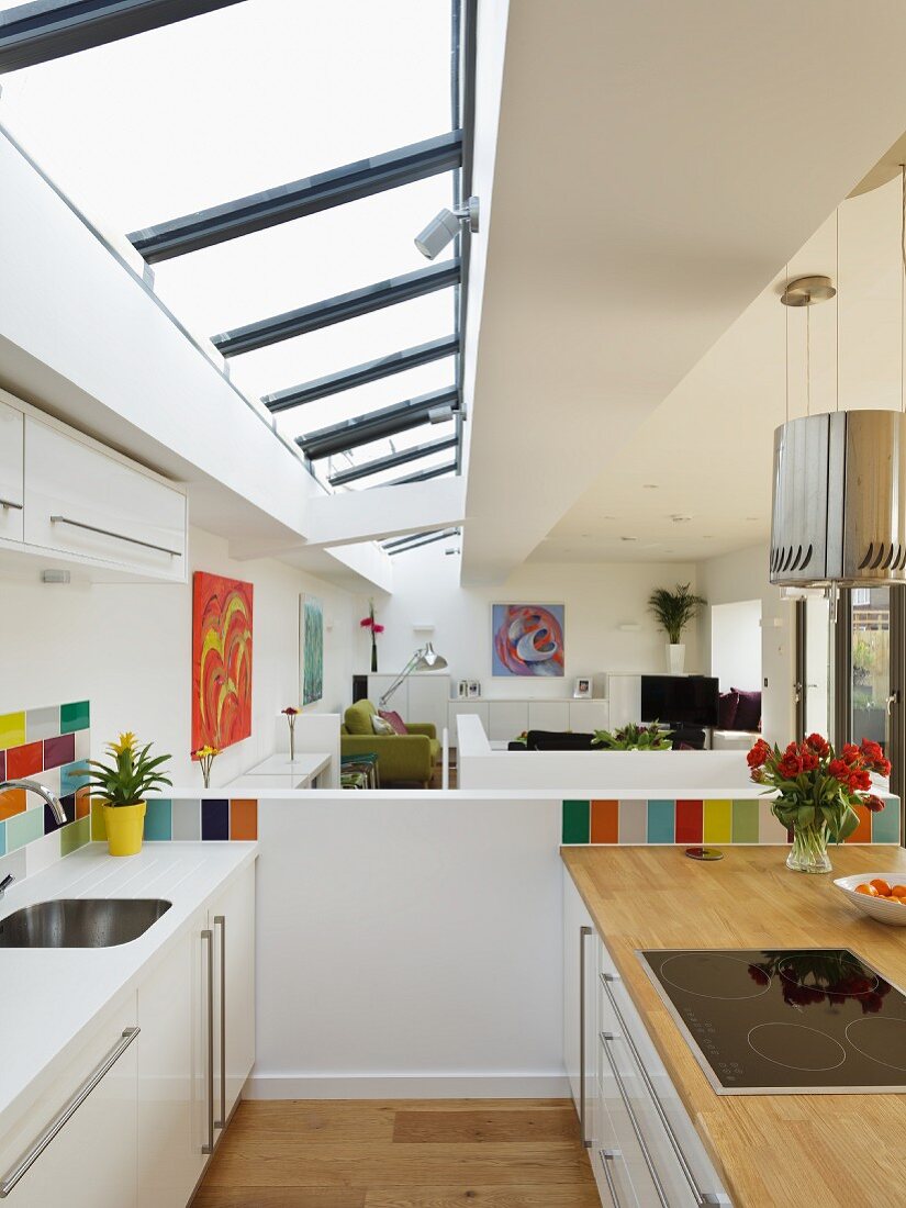 Designer kitchen with colourful wall tiles below skylight in modern, open-plan interior