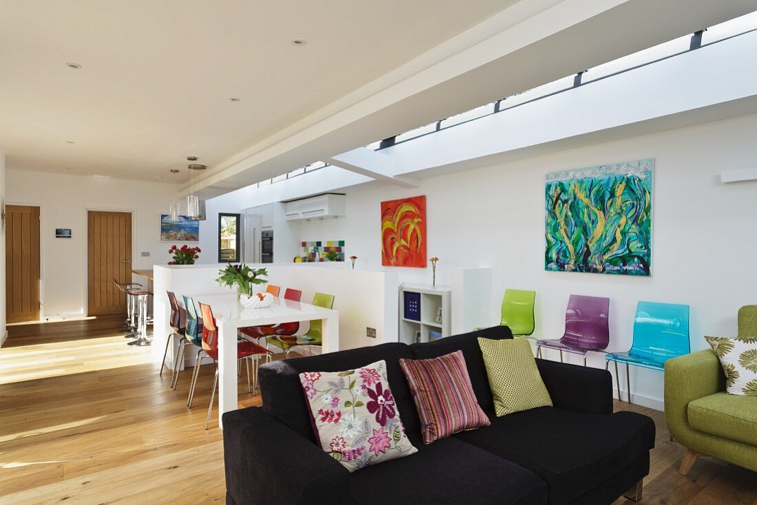 Scatter cushions on black couch in front of dining area in open-plan interior with transom ribbon window