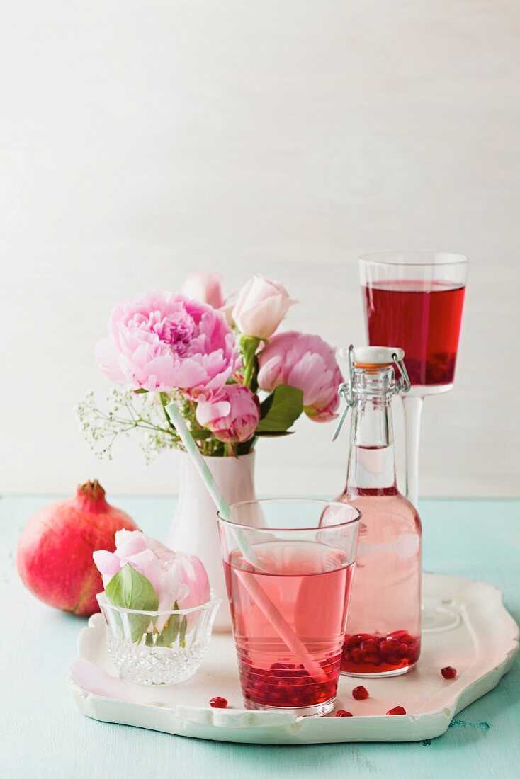 Pomegranate lemonade, syrup, pomegranate seeds and peonies on a tray