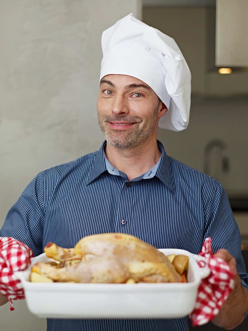 A chef presenting a roast chicken in the roasting dish