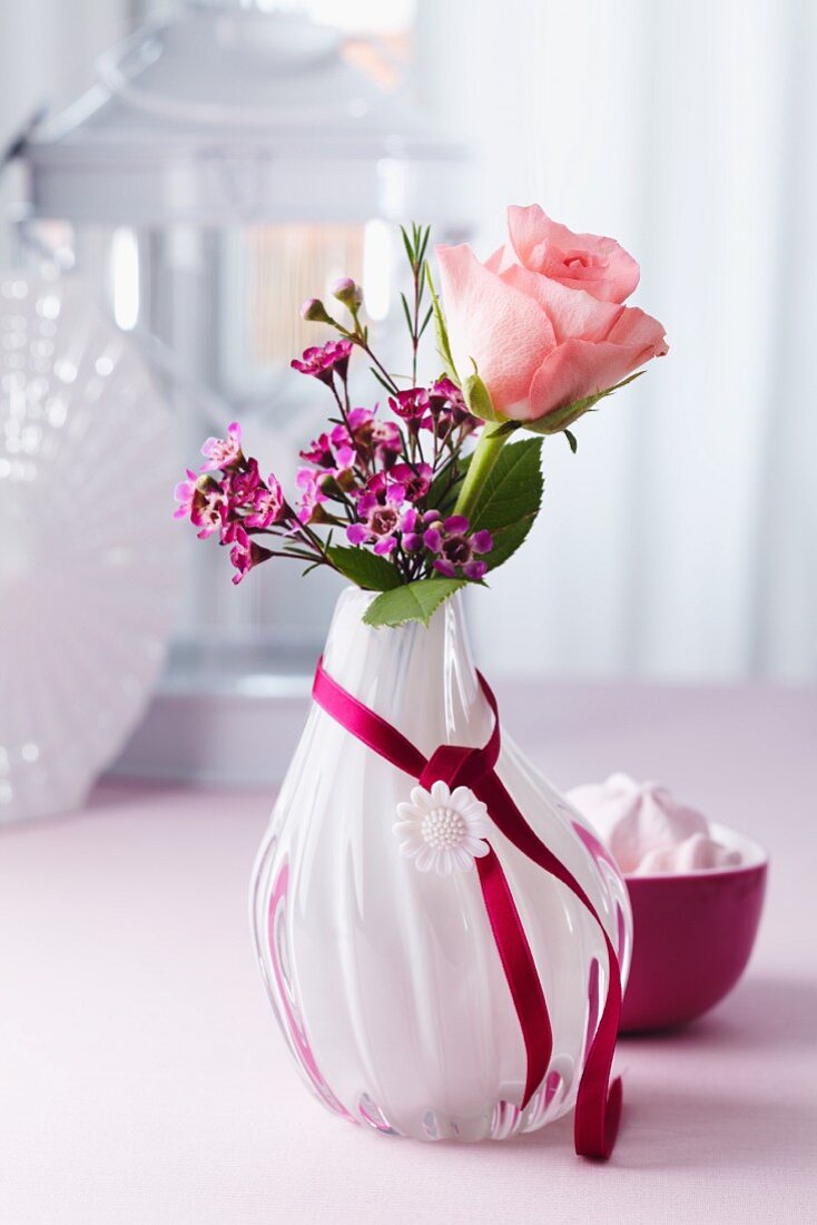 Rose & waxflowers in glass vase decorated with satin ribbon & button