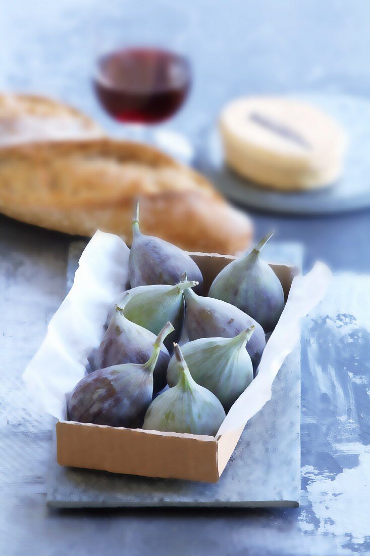 Figs in a box, with bread, cheese and wine in the background