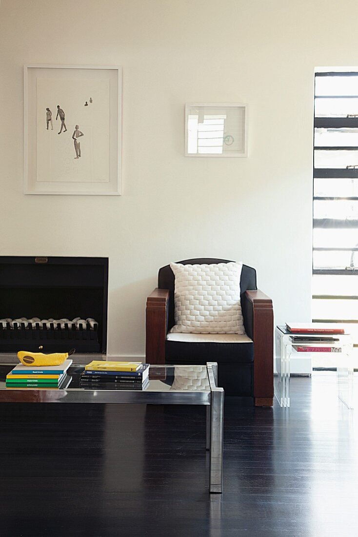 Minimalist artworks on wall above retro armchair and glass and metal coffee table