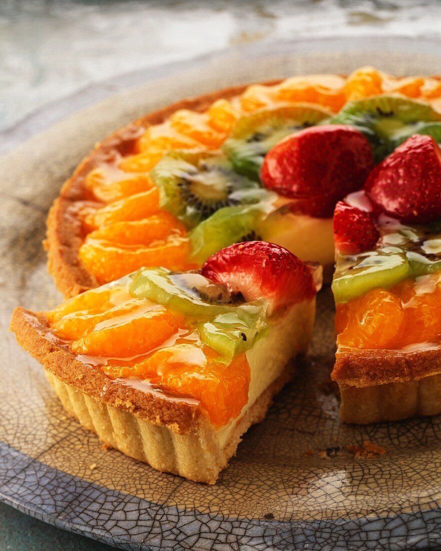 Fruit tart topped with mandarins and strawberries, with one slice cut