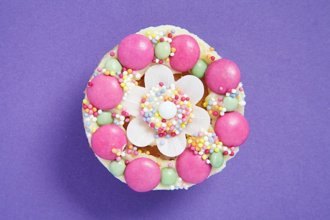 Cupcake mit bunten Schokolinsen und Zuckerstreuseln dekoriert