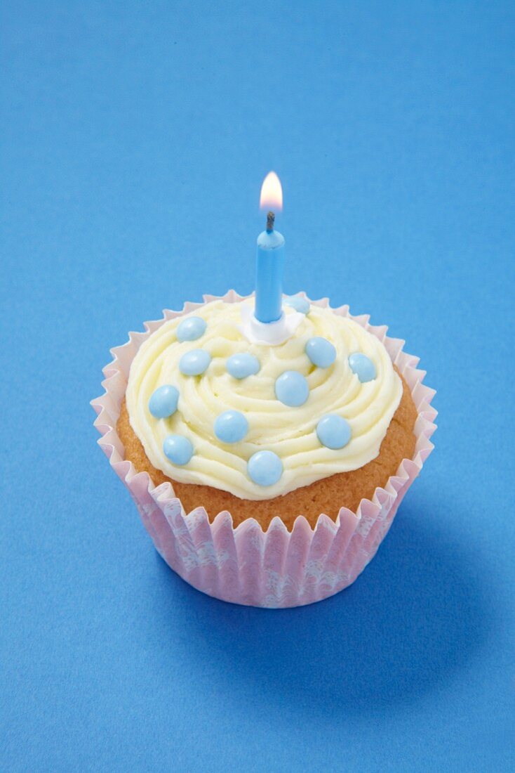 Cupcake mit hellblauen Schokolinsen und einer Kerze