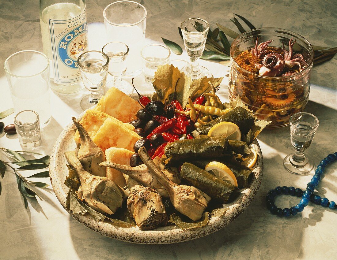Several Greek Appetizers on Plate, Bowl with pickled Squid and Bottle of Ouzo with Glasses