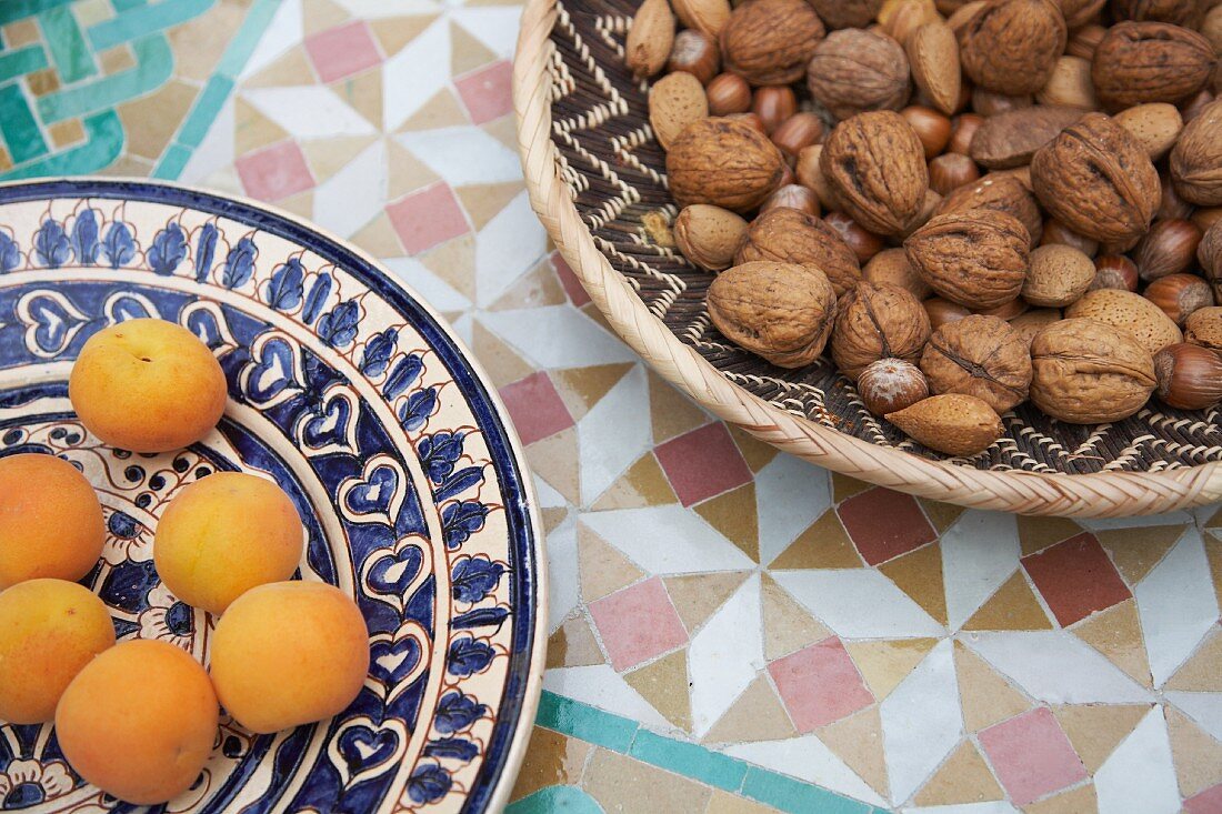 Aprikosen auf Keramikteller, verschiedene Nüsse im Korb