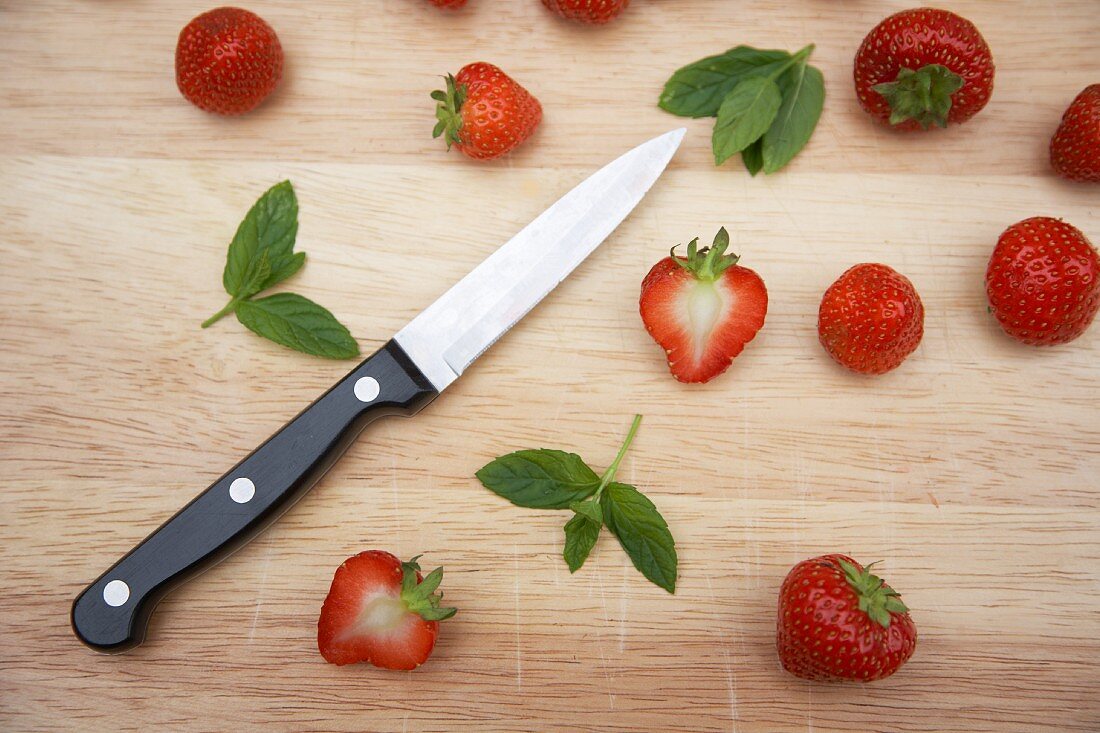 Frische Erdbeeren, Minzeblättchen und Messer auf Holzbrett