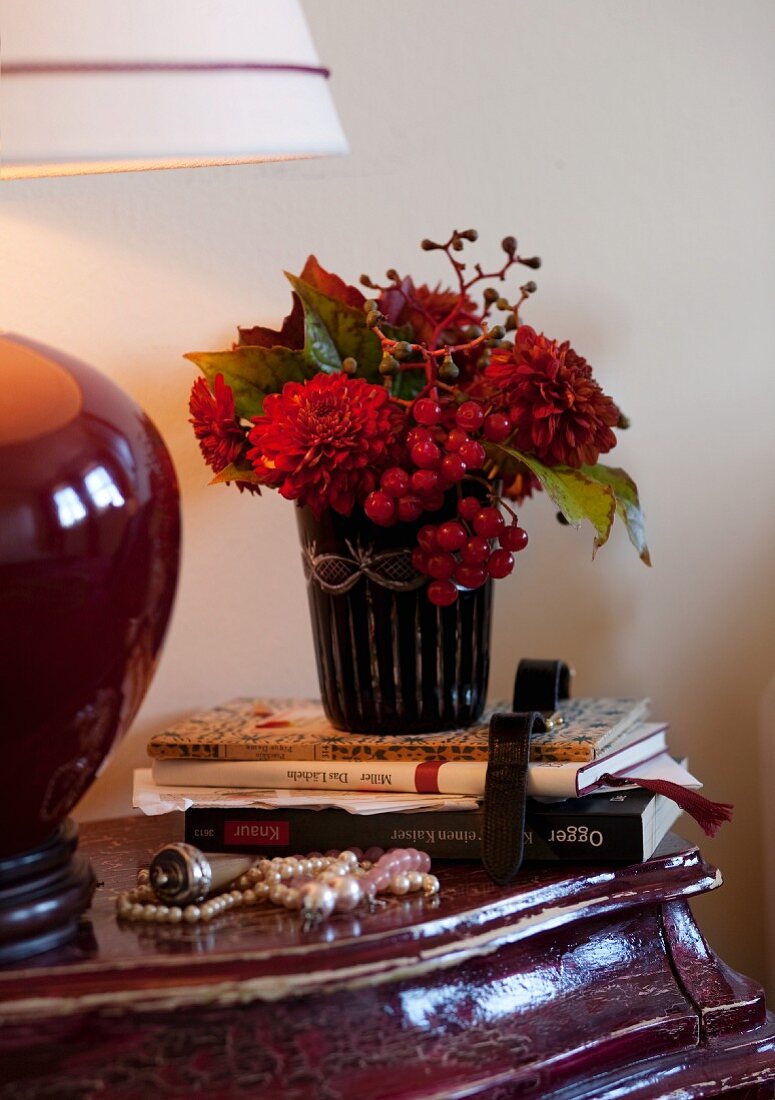 Herbstlicher Blumenstrauss, Bücher, Perlenkette und Lampe auf einem Nachttisch im Barockstil