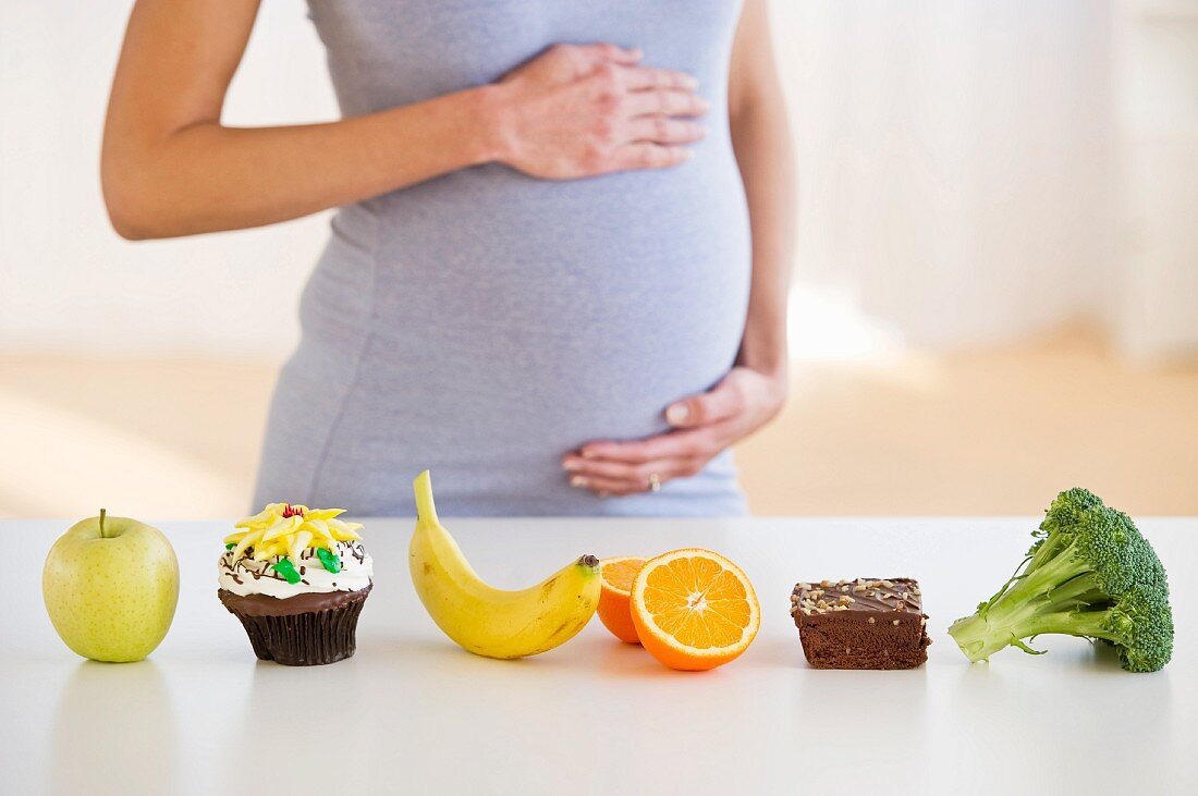 Schwangere Frau steht hinter einer Reihe von Lebensmitteln