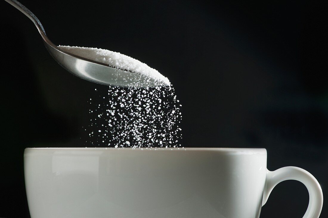 Zucker in eine Kaffeetasse schütten